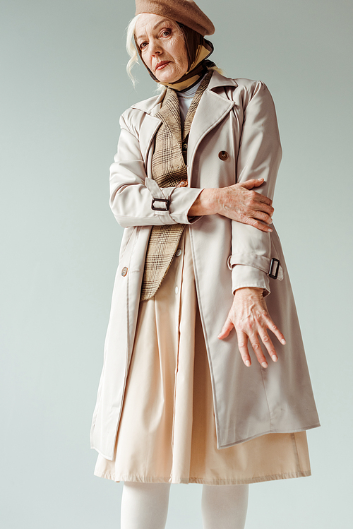 Senior woman in beret and trench coat  isolated on grey