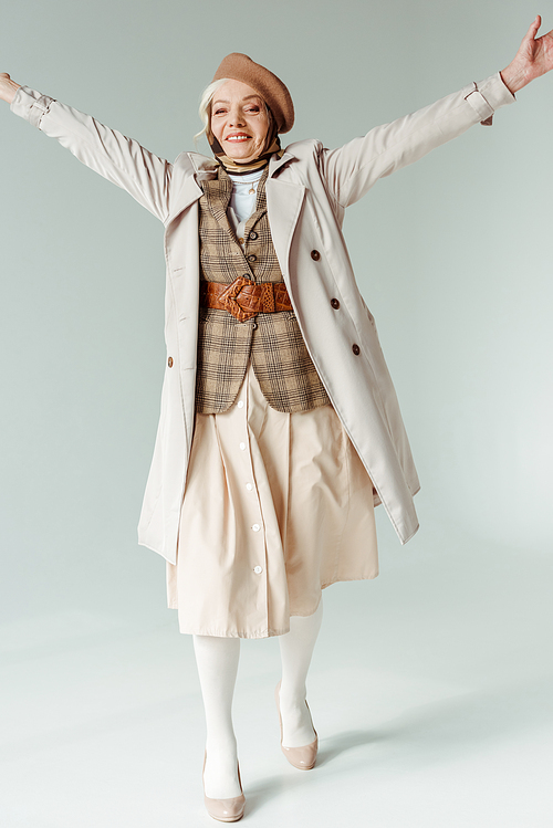 Full length of stylish senior woman with raised hands smiling at camera on white background