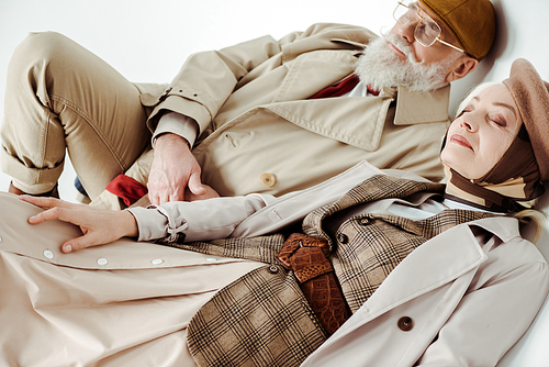 Elegant senior couple in trench coats lying on white background