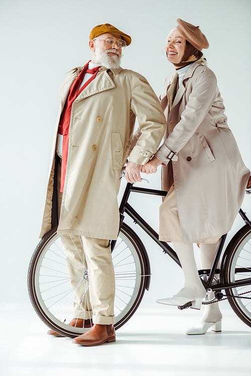 Full length of elegant senior couple with bicycle smiling at each other on white background