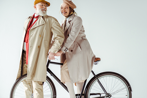 Stylish senior couple smiling at each other near bicycle isolated on white