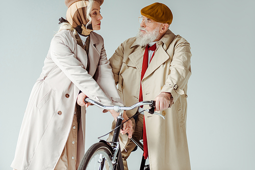 Elegant senior couple looking at each other near bicycle isolated on grey