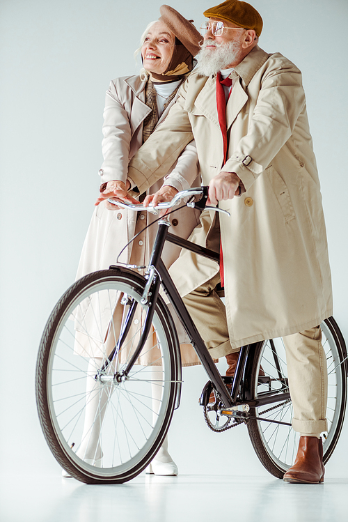 Full length of elegant senior woman smiling away near handsome man on bicycle on white background