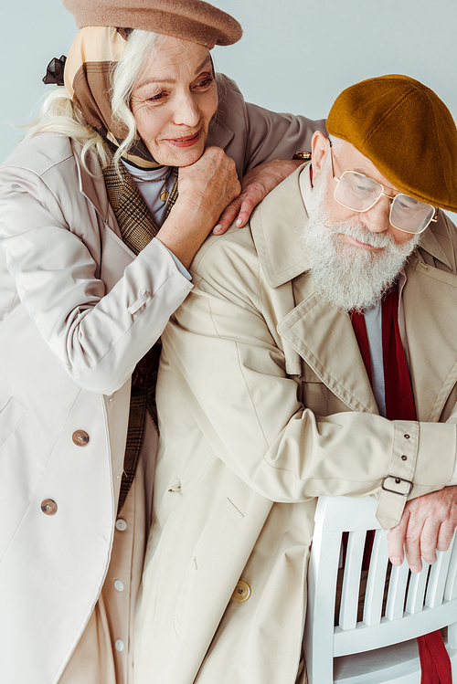 Smiling senior woman embracing stylish man on chair isolated on grey