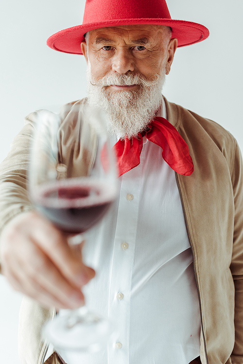 Selective focus of handsome senior man in rd hat holding glass of wine isolated on grey