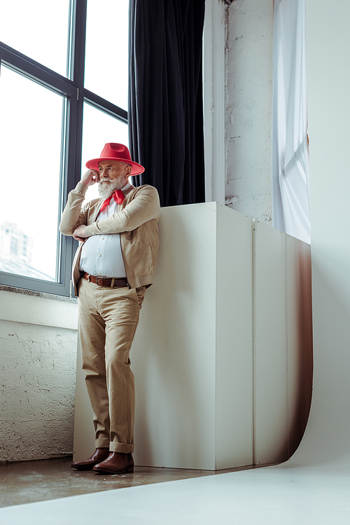 Stylish senior man standing near window in photo studio