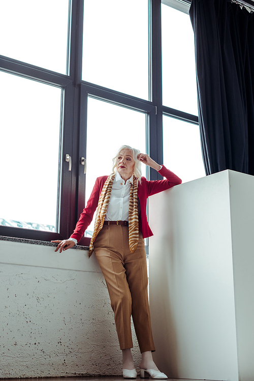 Full length of elegant senior woman standing near window in photo studio