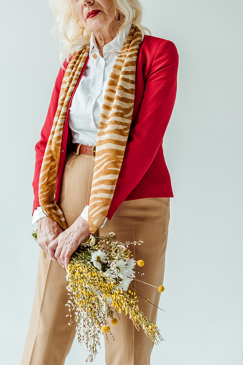 Cropped view of stylish senior woman holding bouquet of wildflowers isolated on grey