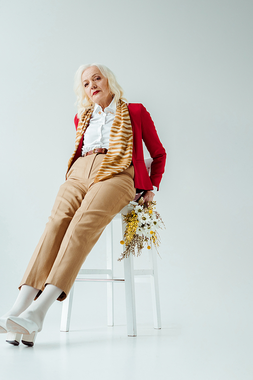 Beautiful elderly woman with wildflowers  on chair on white background