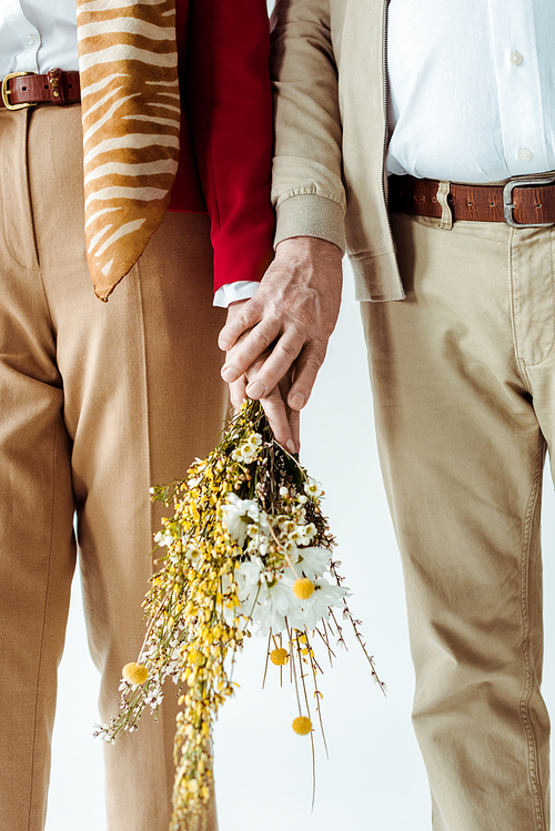 Cropped view of stylish elderly couple holding bouquet of wildflowers isolated on white