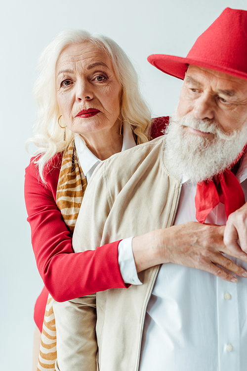 Selective focus of elegant senior woman embracing handsome man in red hat isolated on white