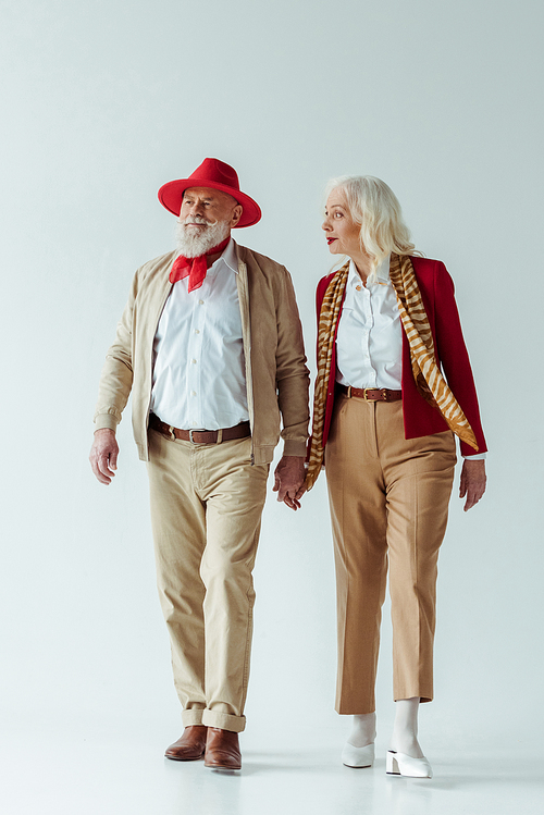 Full length of stylish elderly couple holding hands on white background