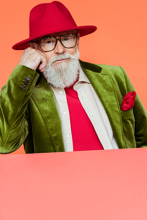 Fashionable elderly man in jacket and eyeglasses  isolated on coral