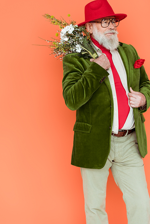 Stylish senior man posing with bouquet of wildflowers isolated on coral