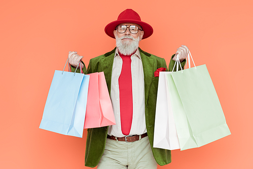 Stylish senior man holding shopping bags and  isolated on coral