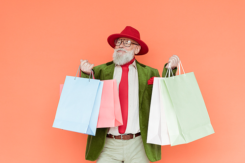 Fashionable elderly man holding shopping bags isolated on coral