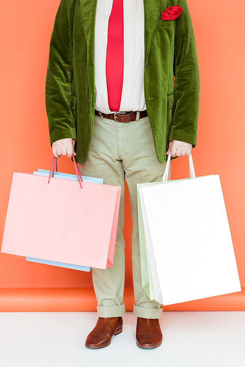 Cropped view of senior man holding shopping bags on white surface on coral background