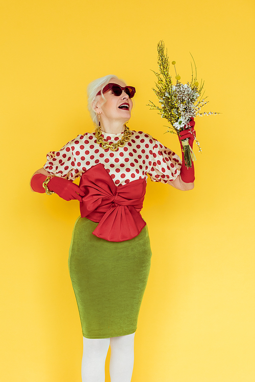 Fashionable elderly woman holding wildflowers isolated on yellow