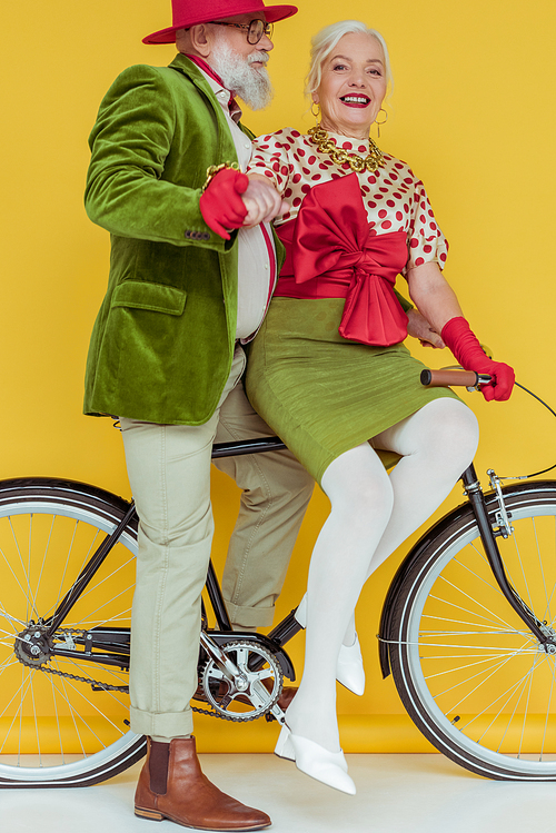 Senior woman smiling at camera near handsome man on bicycle on white surface on yellow background