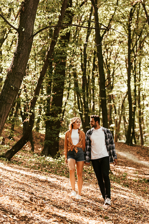 smiling young couple holding hands and looking at each other while walking in park