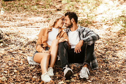 happy young couple sitting face to face on autumn leaves in park