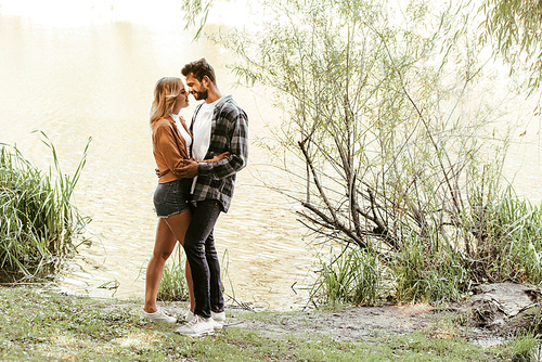 happy young couple embracing while standing near lake in park