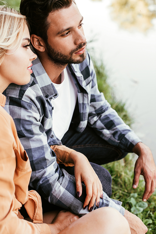 dreamy young couple looking away while spending time near lake