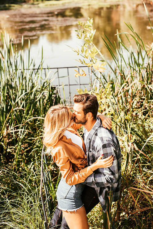 happy young couple embracing and kissing in thicket of sedge near lake