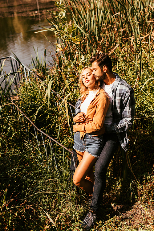 handsome young man embracing attractive girlfriend in thicket of sedge in park