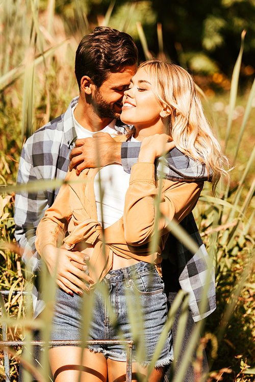 young man embracing happy girlfriend in thicket of sedge in park