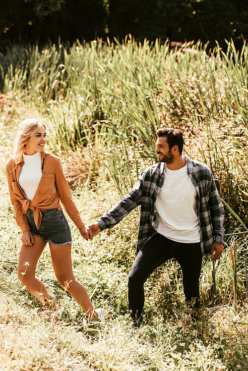 happy young couple holding hands while walking in thicket of sedge