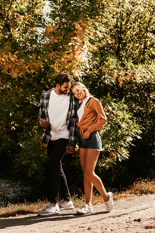 happy young woman leaning on shoulder of boyfriend while walking in park