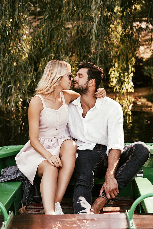 happy young couple kissing while sitting in boat on lake