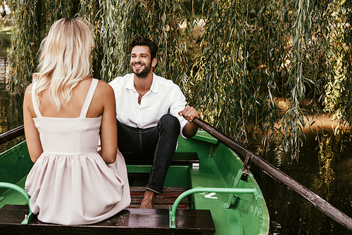 back view of young woman sitting in boat near happy boyfriend