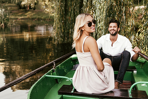 cheerful young woman  while sitting in boat near happy boyfriend