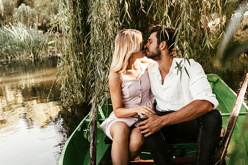 happy young couple kissing while sitting in boat on lake