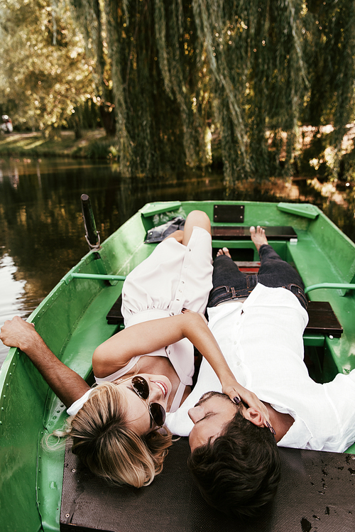 overhead view of young woman touching face of boyfriend while lying in boat