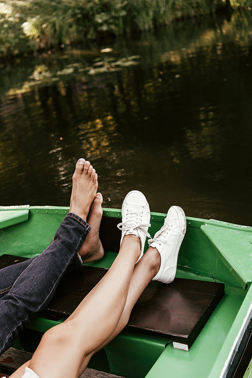 cropped view of barefoot man and girl in sneakers relaxing in boat on lake