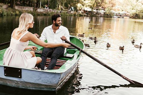 happy young couple in boat on lake near flack of ducks