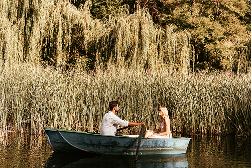 young couple in boat on river near thicket of sedge