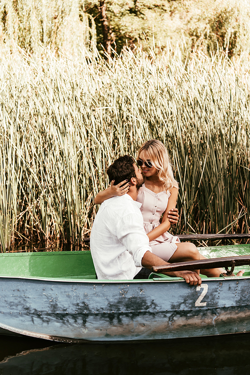 young couple embracing and kissing in boat on river near thicket of sedge