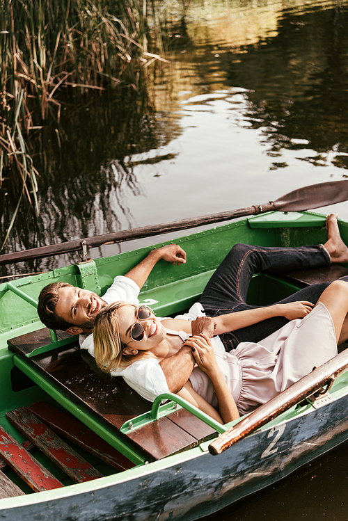 happy young couple relaxing in boat on lake and smiling at camera