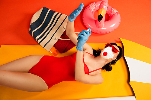 woman in sunglasses, medical mask, latex gloves and swimsuit applying hand sanitizer on orange