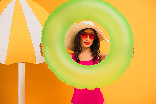 stylish woman in straw hat, sunglasses and swimsuit holding inflatable ring on yellow