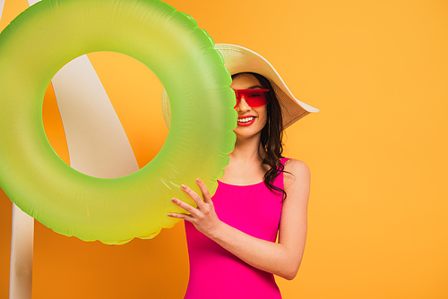 happy woman in straw hat, sunglasses and swimsuit holding inflatable ring on yellow