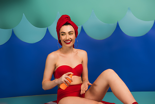 happy woman in red towel and swimsuit applying sunscreen near paper cut waves