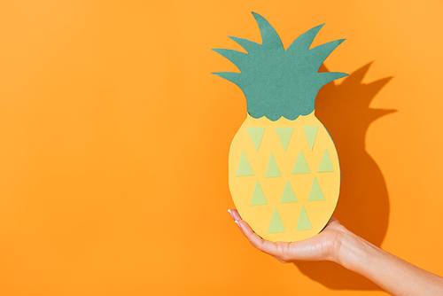 cropped view of woman holding paper cut pineapple on orange