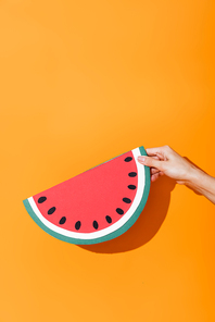 cropped view of girl holding paper cut watermelon on orange