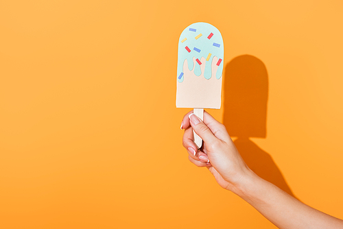 cropped view of young woman holding paper cut ice cream on orange