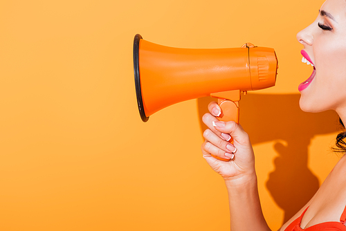 side view of young woman screaming in megaphone on orange